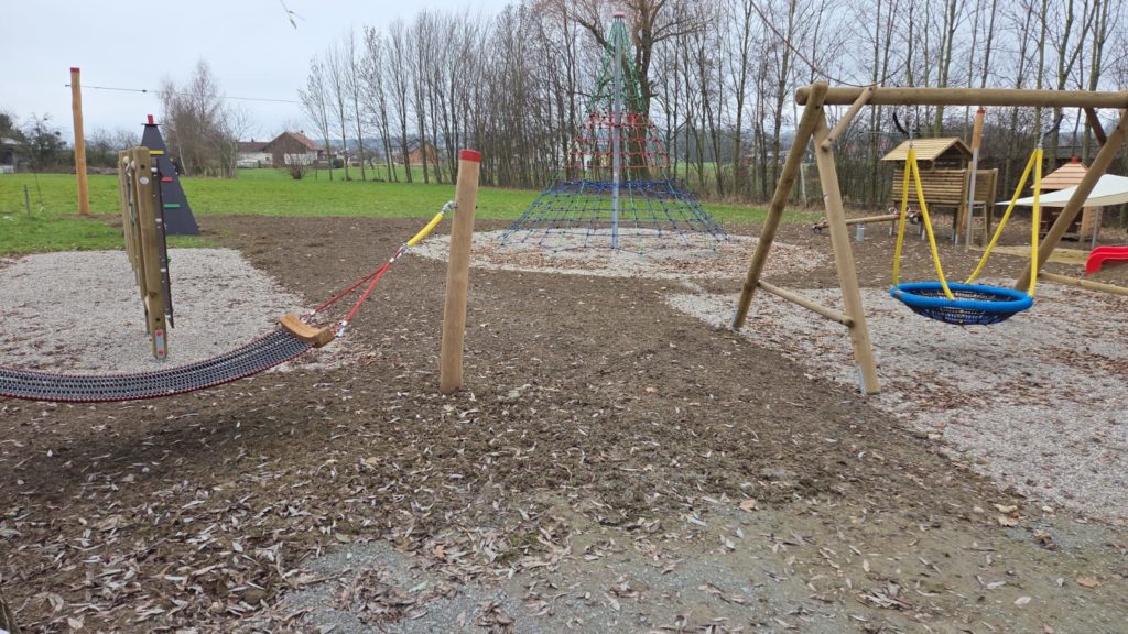 Spielplatz mit großer Liege-Hängematte und einer Kletterwand im Hintergrund.